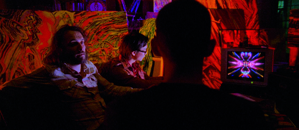 People and a television in a room lit with saturated red and violet colours in Enter the Void.